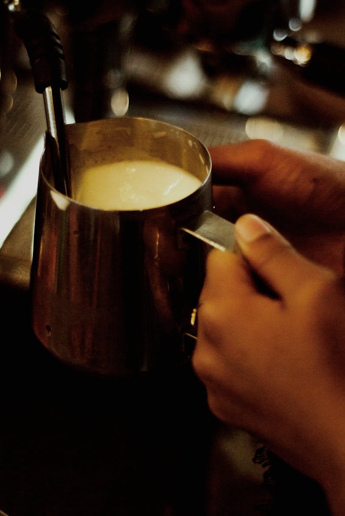 Barista steaming milk in a metal jug, creating creamy foam for a perfect coffee beverage.