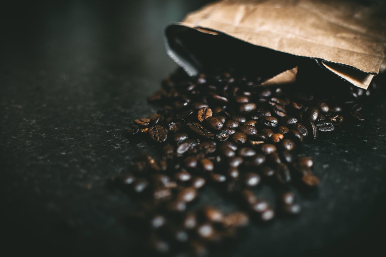 Close-up of roasted coffee beans spilling from brown paper bag, exuding warmth and aroma.